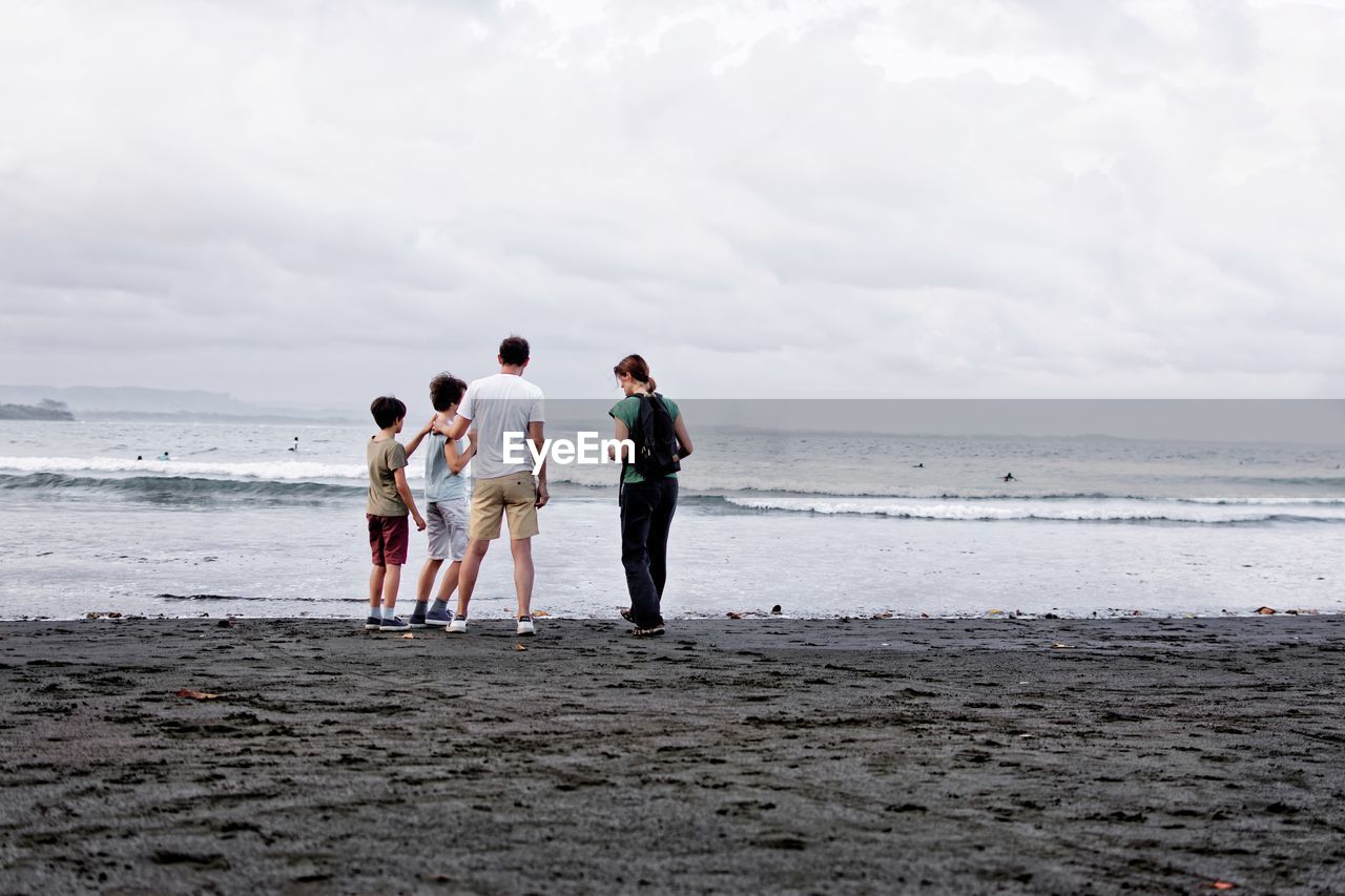 Family standing on shore at beach against sky