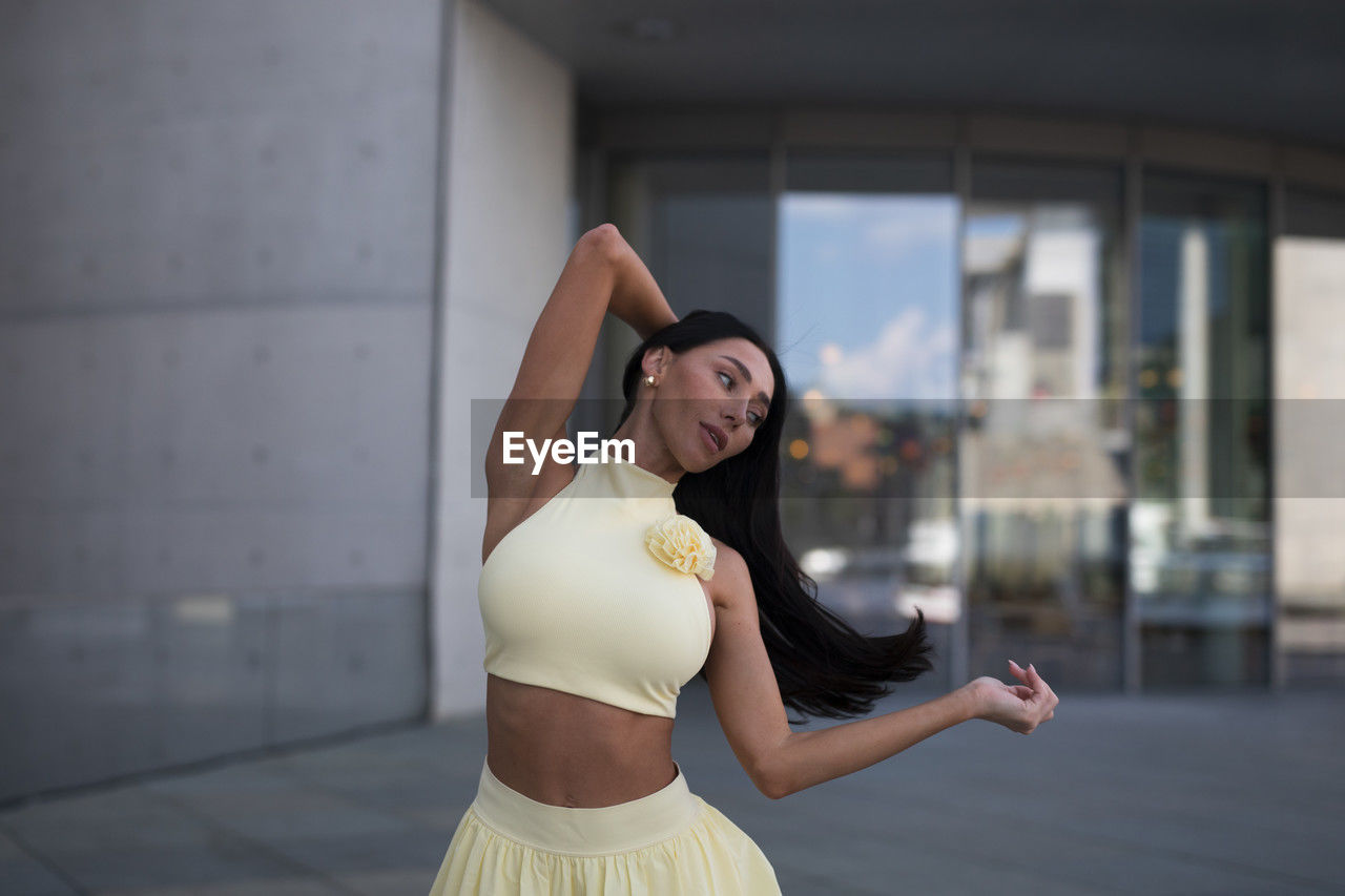 one person, adult, women, young adult, clothing, lifestyles, hairstyle, exercising, dancing, city, fashion, long hair, dress, architecture, standing, arm, wellbeing, brown hair, city life, arms raised, photo shoot, limb, female, sports, portrait, looking, person, focus on foreground, vitality, outdoors, human limb, ballet, side view, arts culture and entertainment, ballet dancer, copy space, elegance, day, leisure activity, happiness, flexibility, emotion