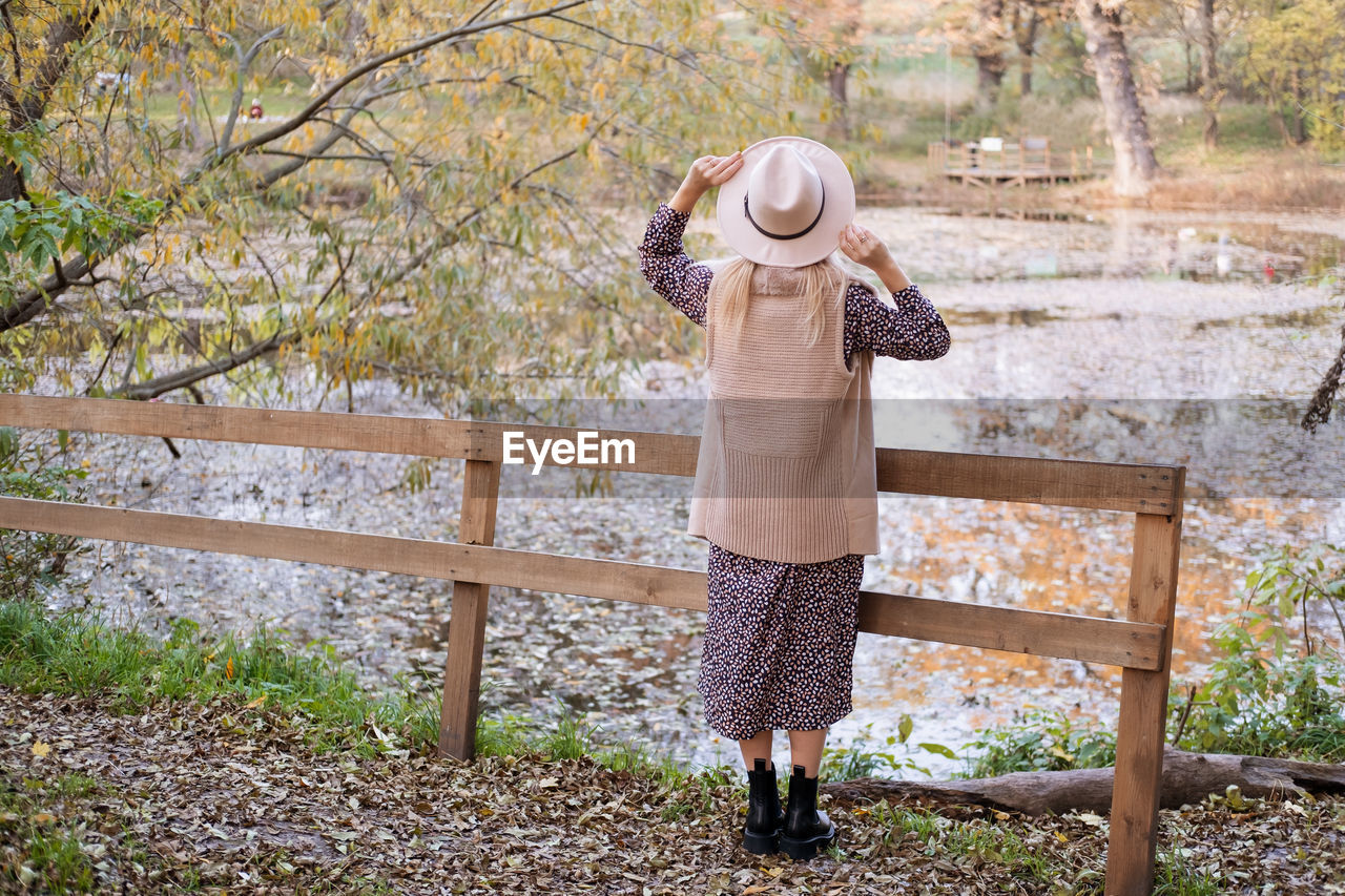 one person, full length, tree, nature, spring, standing, casual clothing, plant, clothing, leisure activity, day, lifestyles, women, wood, adult, outdoors, autumn, childhood, hat, child, fence, person, holding, land, rear view, landscape, female, woodland