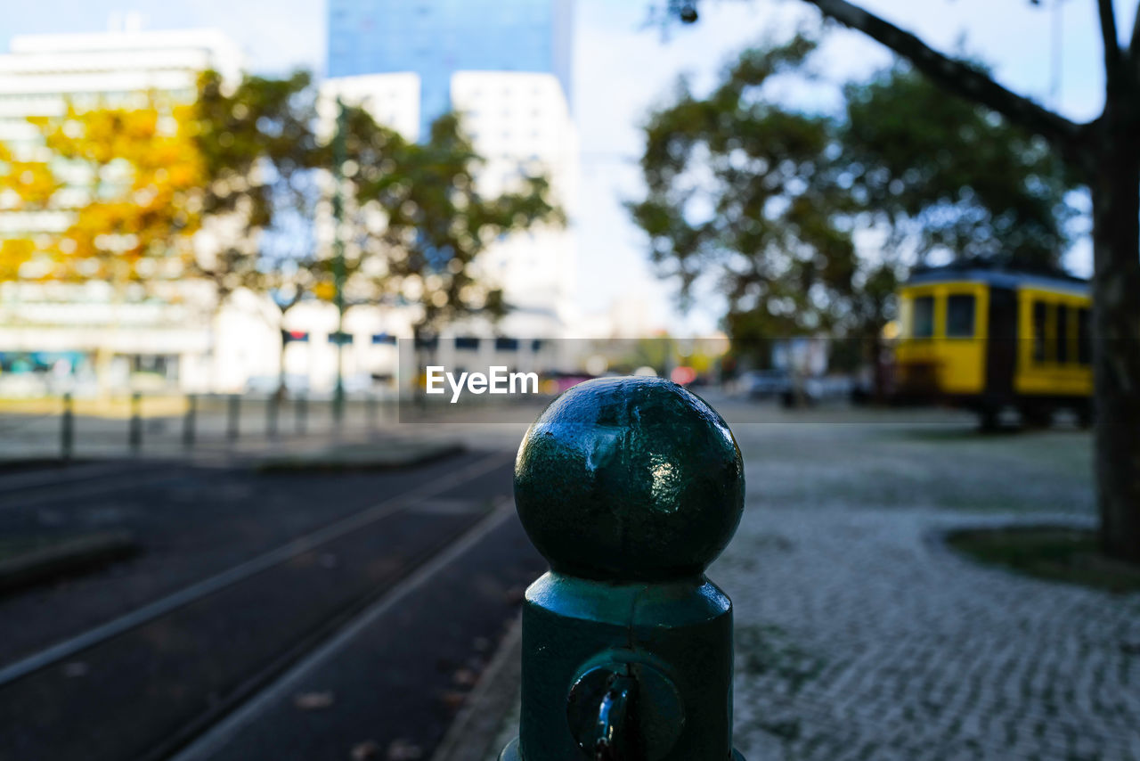 city, focus on foreground, transportation, street, architecture, blue, day, no people, mode of transportation, vehicle, nature, tree, road, outdoors, plant, building exterior, built structure, close-up, city life, sky, light, rail transportation, lighting