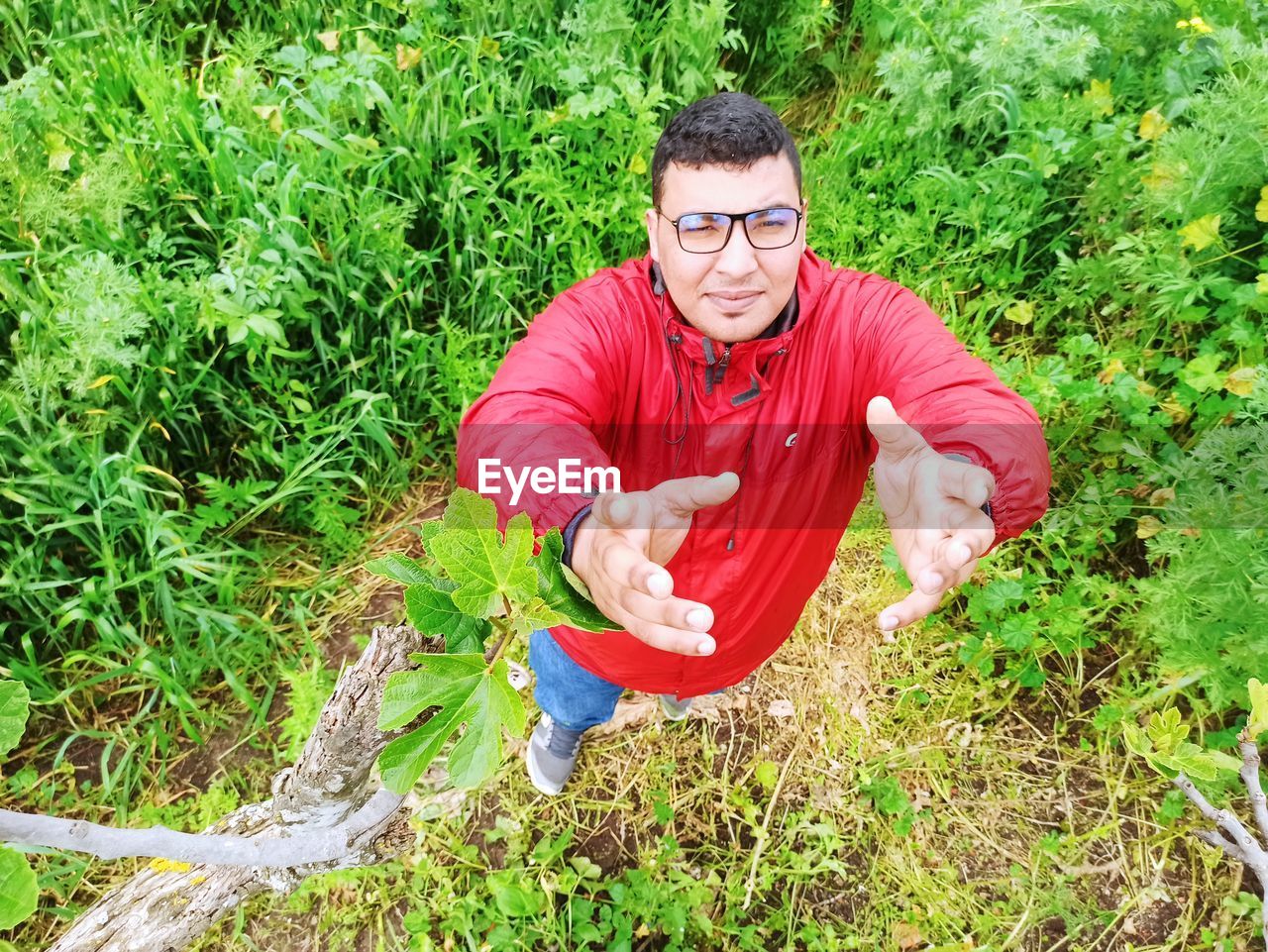 plant, one person, glasses, men, nature, grass, adult, eyeglasses, lifestyles, green, leisure activity, land, portrait, looking at camera, front view, casual clothing, day, growth, young adult, field, outdoors, red, flower, smiling, high angle view, full length, agriculture, sitting, natural environment, forest