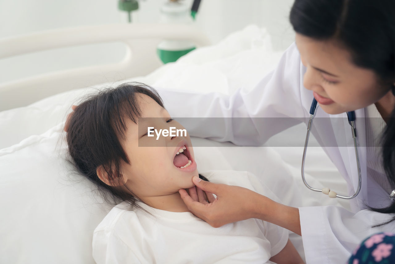 Woman doctor examining little girl mouth at hospital checking the sore throat of a young patient