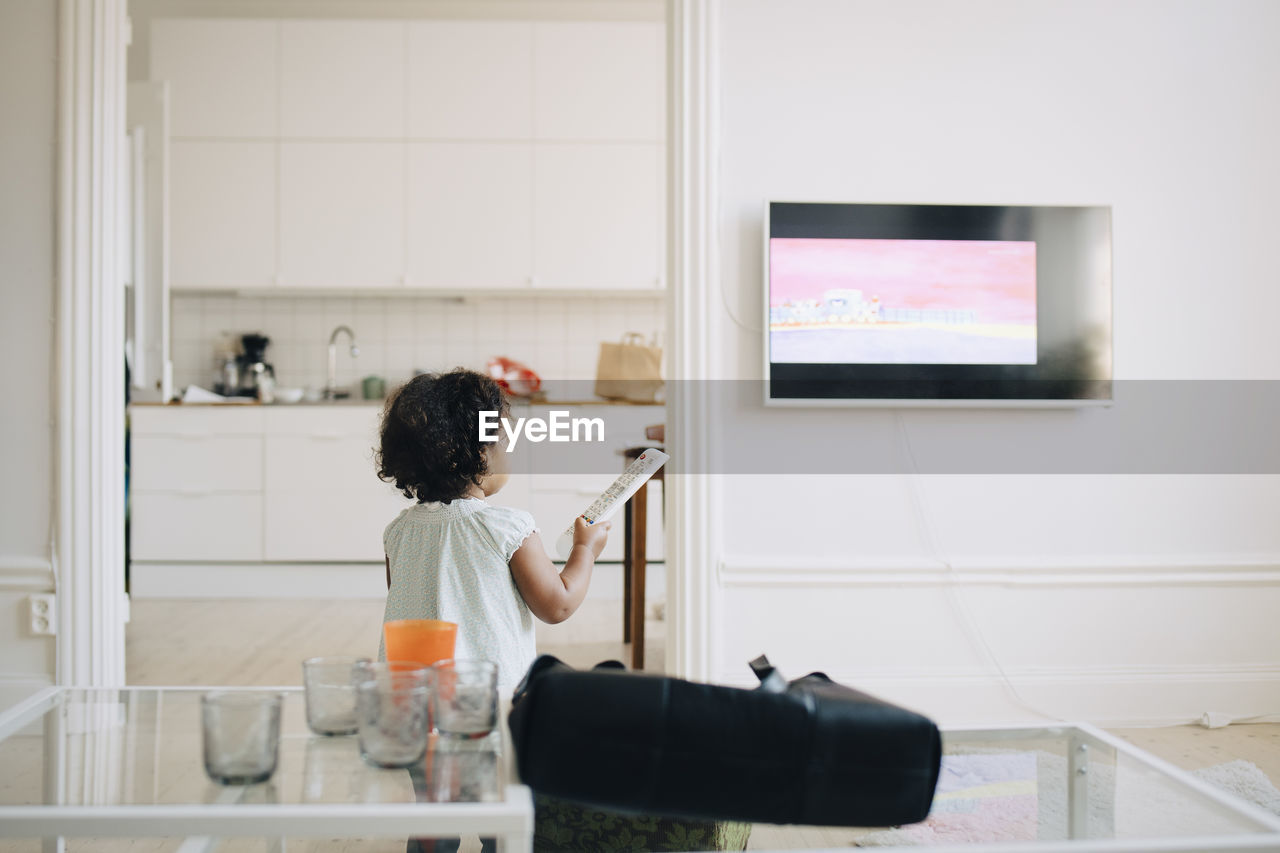 Rear view of girl with remote control watching tv at home