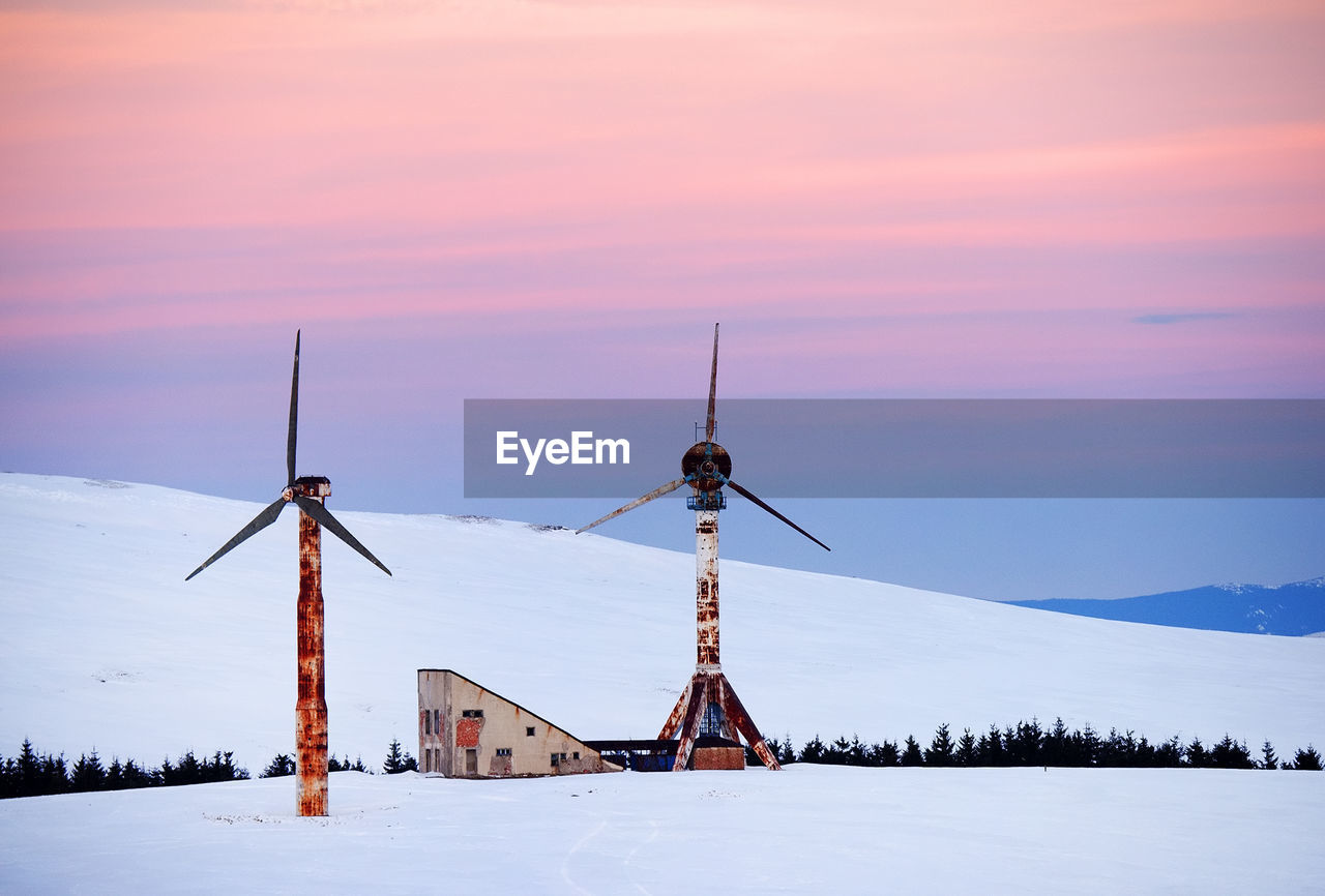 Windmills on snow covered landscape against sky during sunset