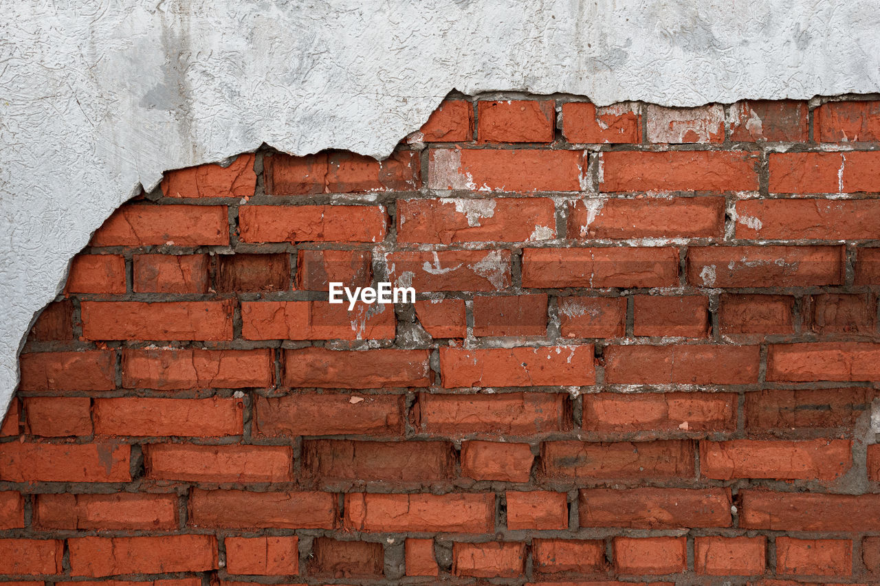 Full frame shot of red brick wall with damaged grey layer of plaster