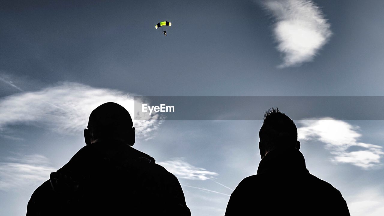 Low angle view of men looking at parachute in sky