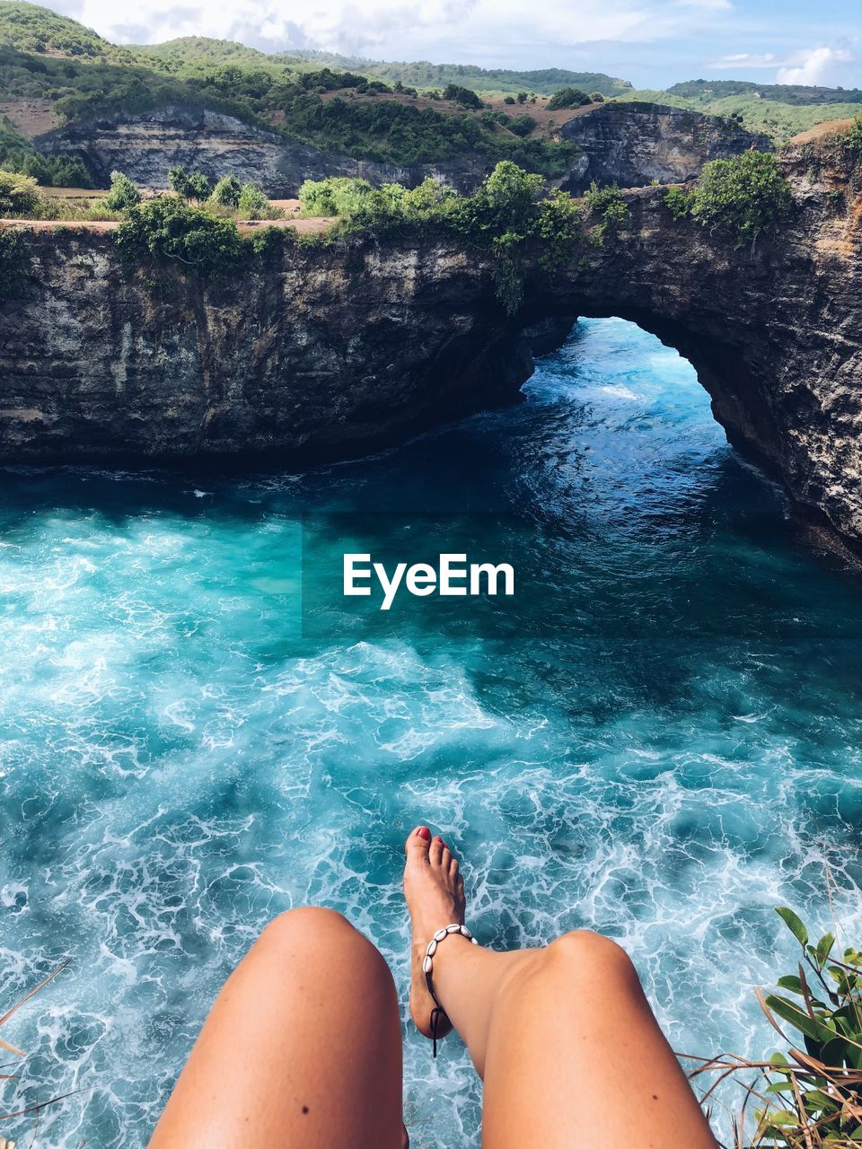 Low section of woman sitting on cliff over sea