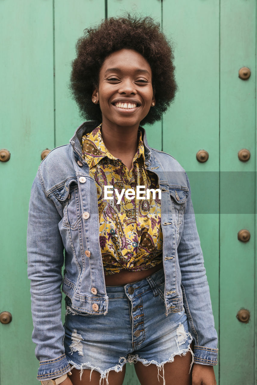 Curly hair woman smiling while standing in front of wall