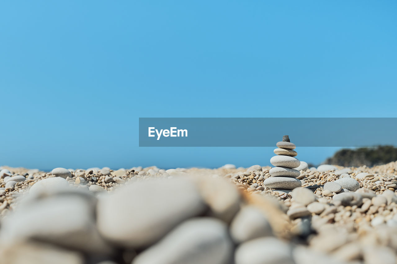 Pyramid stones balance on the beach against a blue bright sky. 