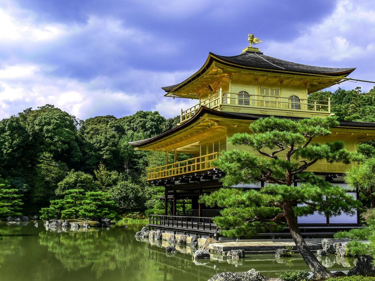 Kinkaku-ji temple by pond against cloudy sky