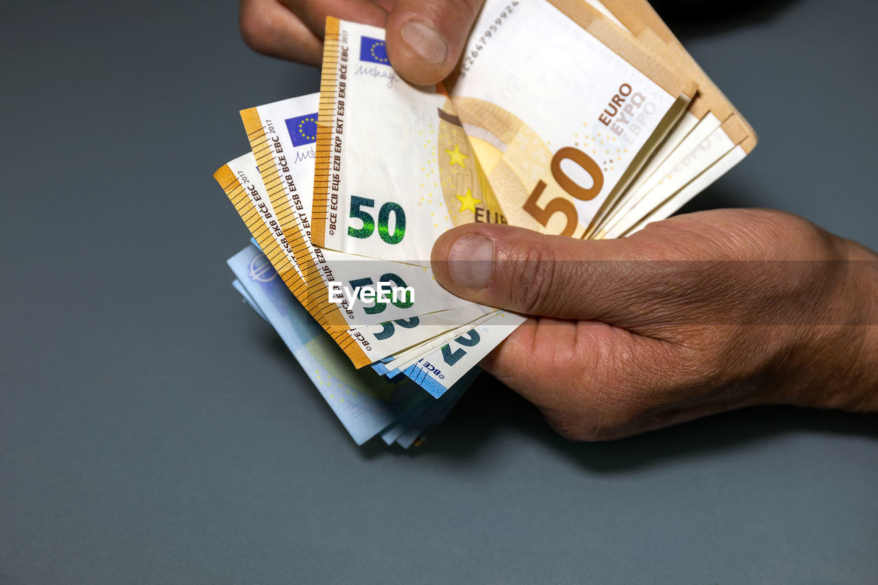 CLOSE-UP OF A HAND HOLDING PAPER OVER COLORED BACKGROUND