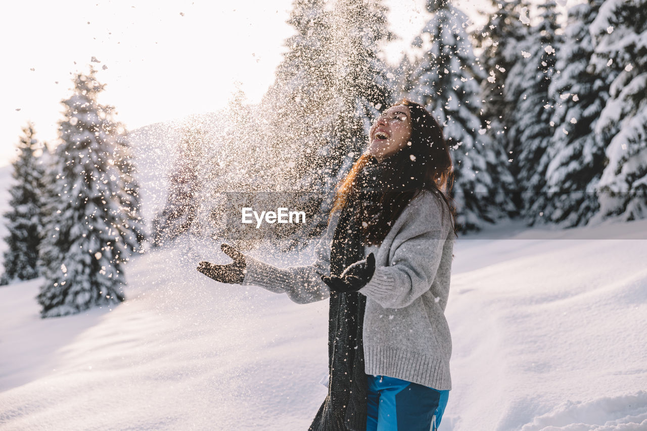 Woman having fun while hiking in the snow during winter, at sunset time.