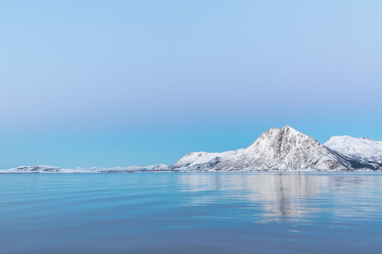 Scenic view of snowcapped mountains by sea against blue sky