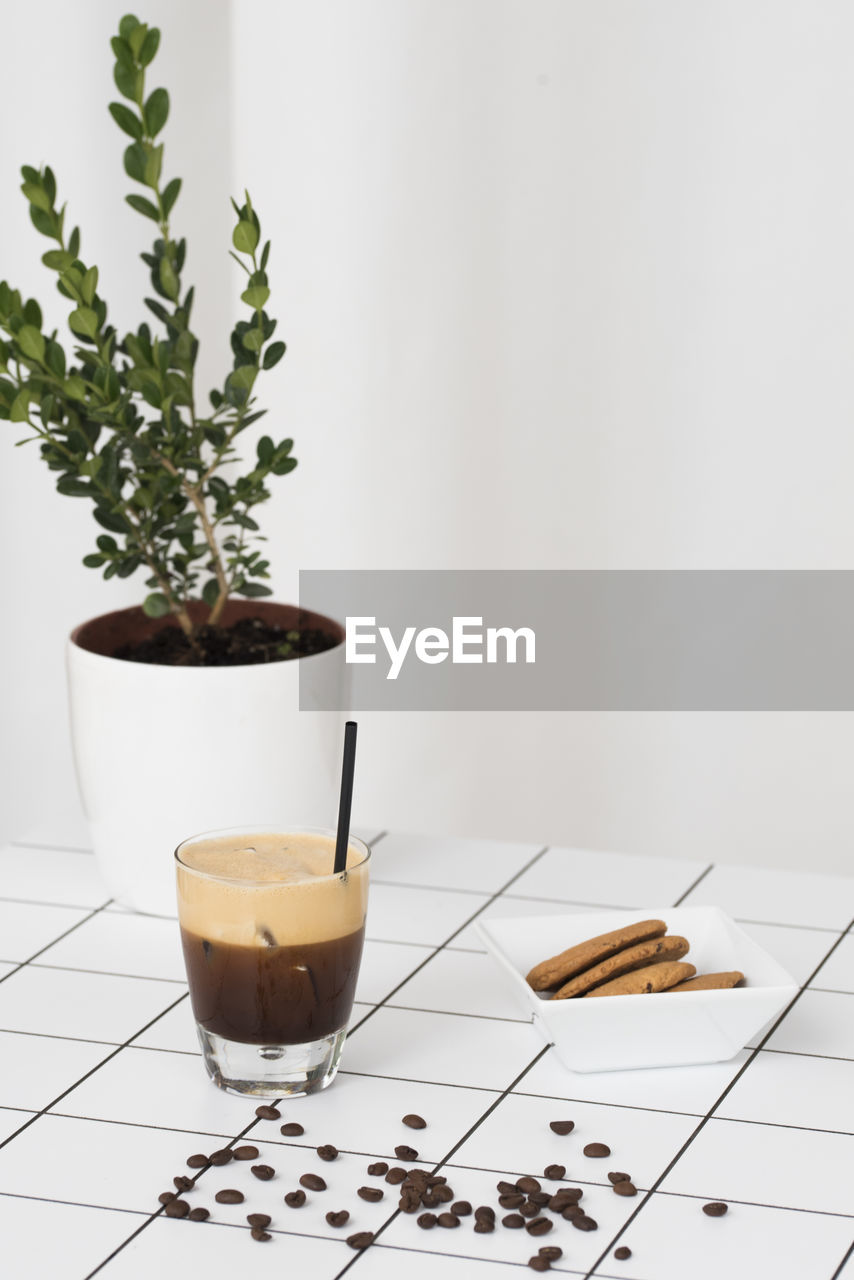 Coffee and biscuits by potted plant on floor against white wall