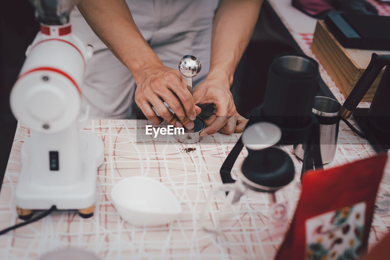 adult, indoors, hand, occupation, working, clothing, table, men, creativity, tableware, one person, cup, red, high angle view, skill, art, business, young adult, person, midsection, mug, selective focus, food and drink, sitting, coffee