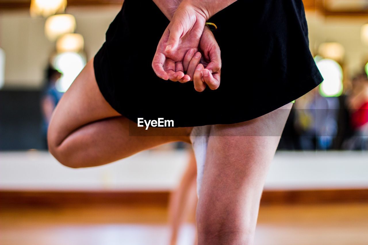 Midsection of woman standing on one leg indoors