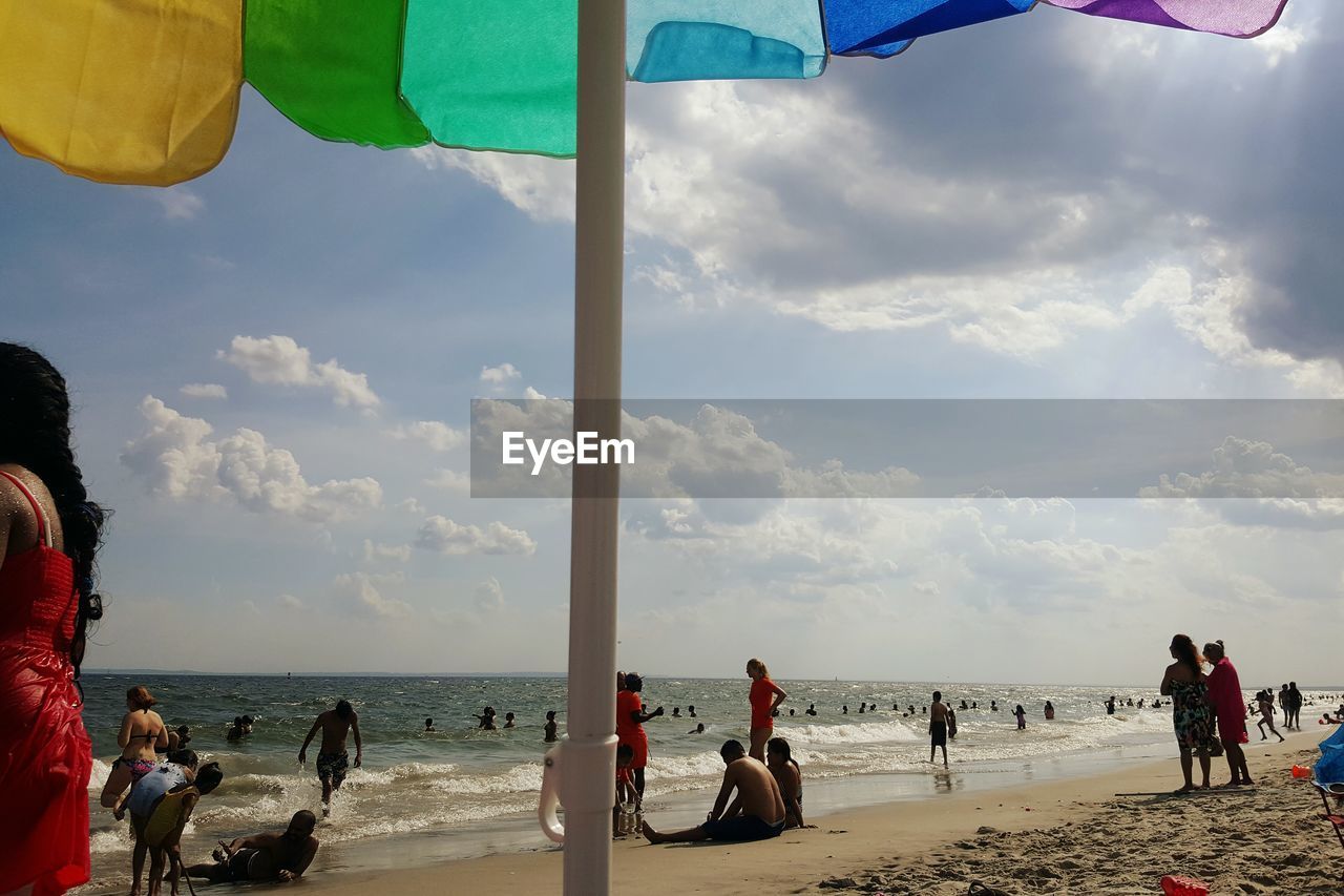 People at beach against cloudy sky