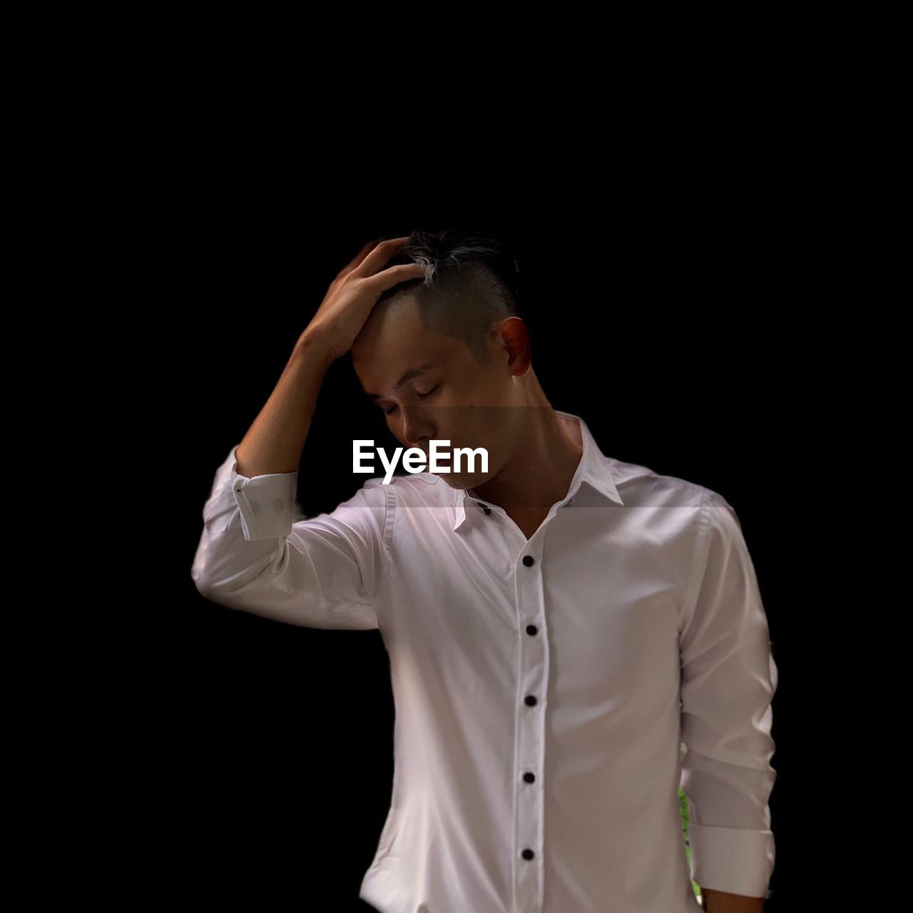 Young man with hand in hair standing against black background