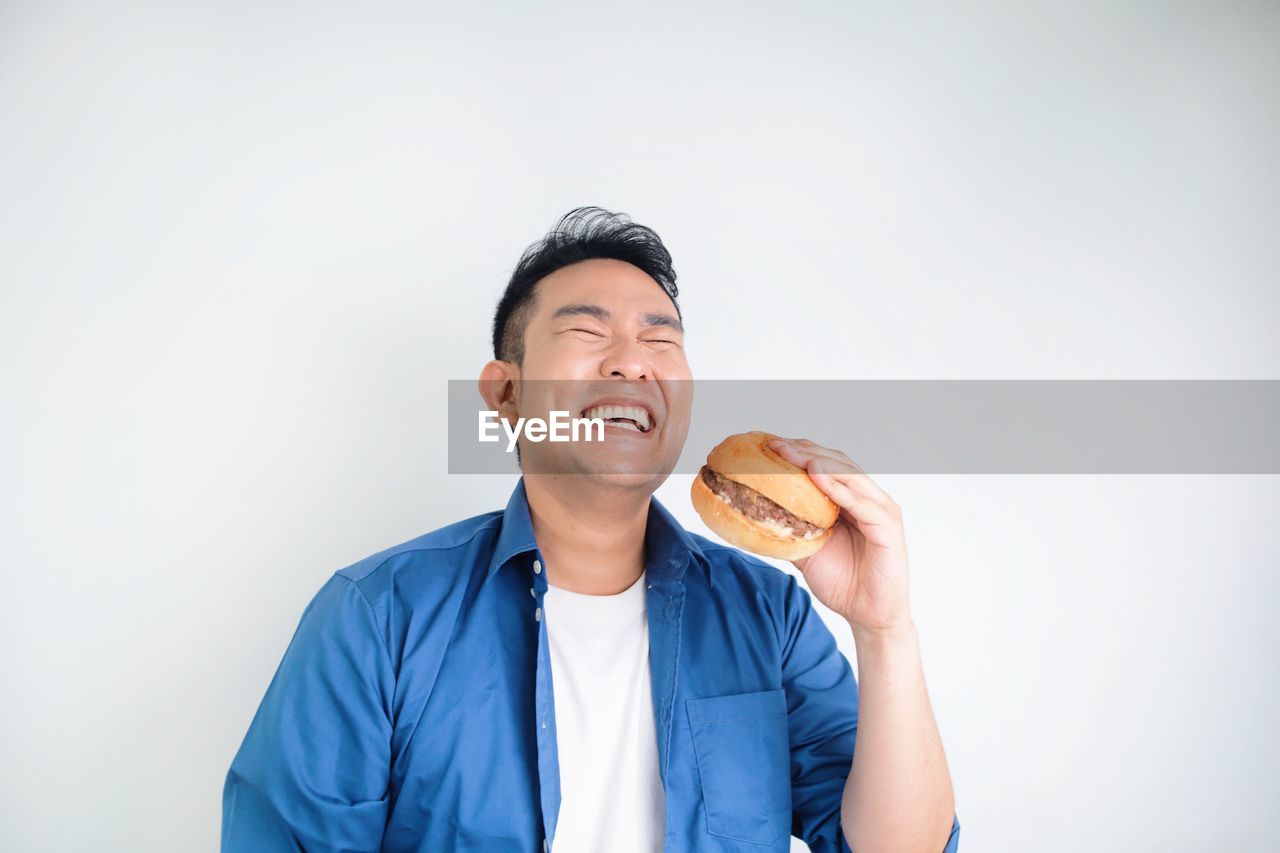 Happy asian man holding beef burger chicken standing over white background with copy space.