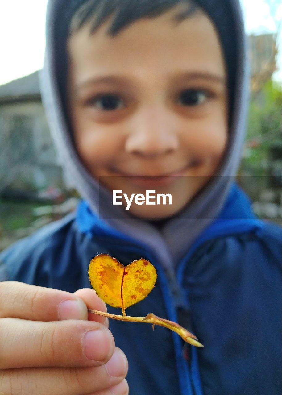 Close-up portrait of smiling boy holding leaf