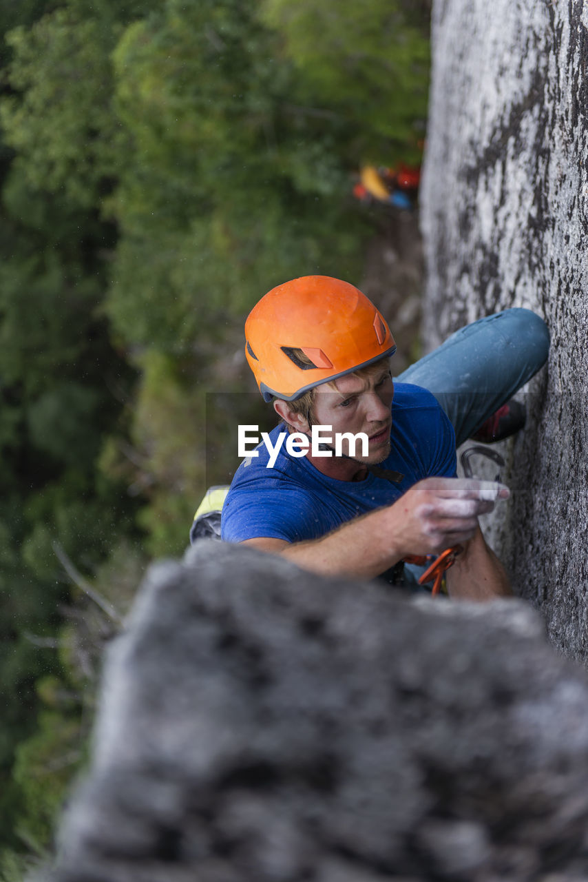 Close-up of man lead climbing and placing gear with helmet and focus