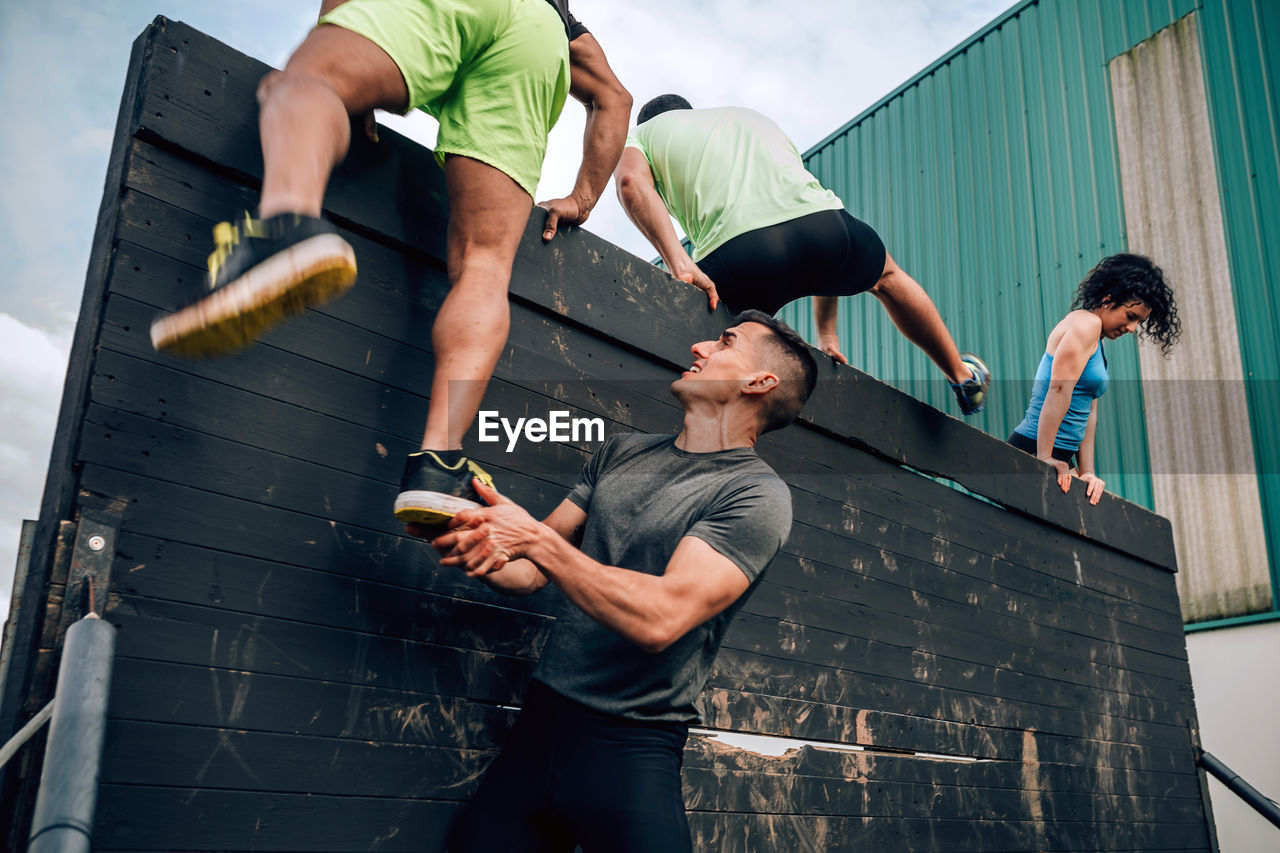 Young man assisting friend while climbing wooden wall