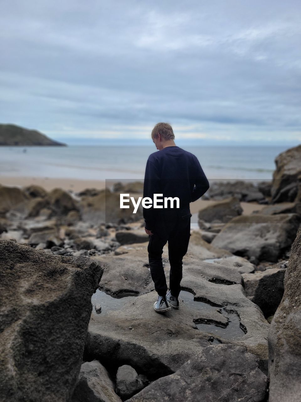 Rear view of man standing on rock against sky