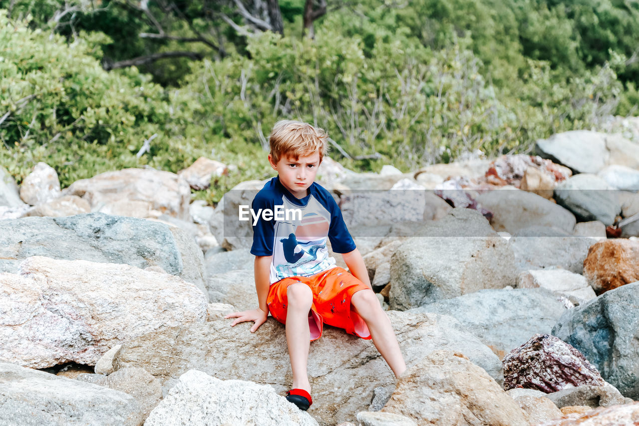 Boy sitting on rock outdoors