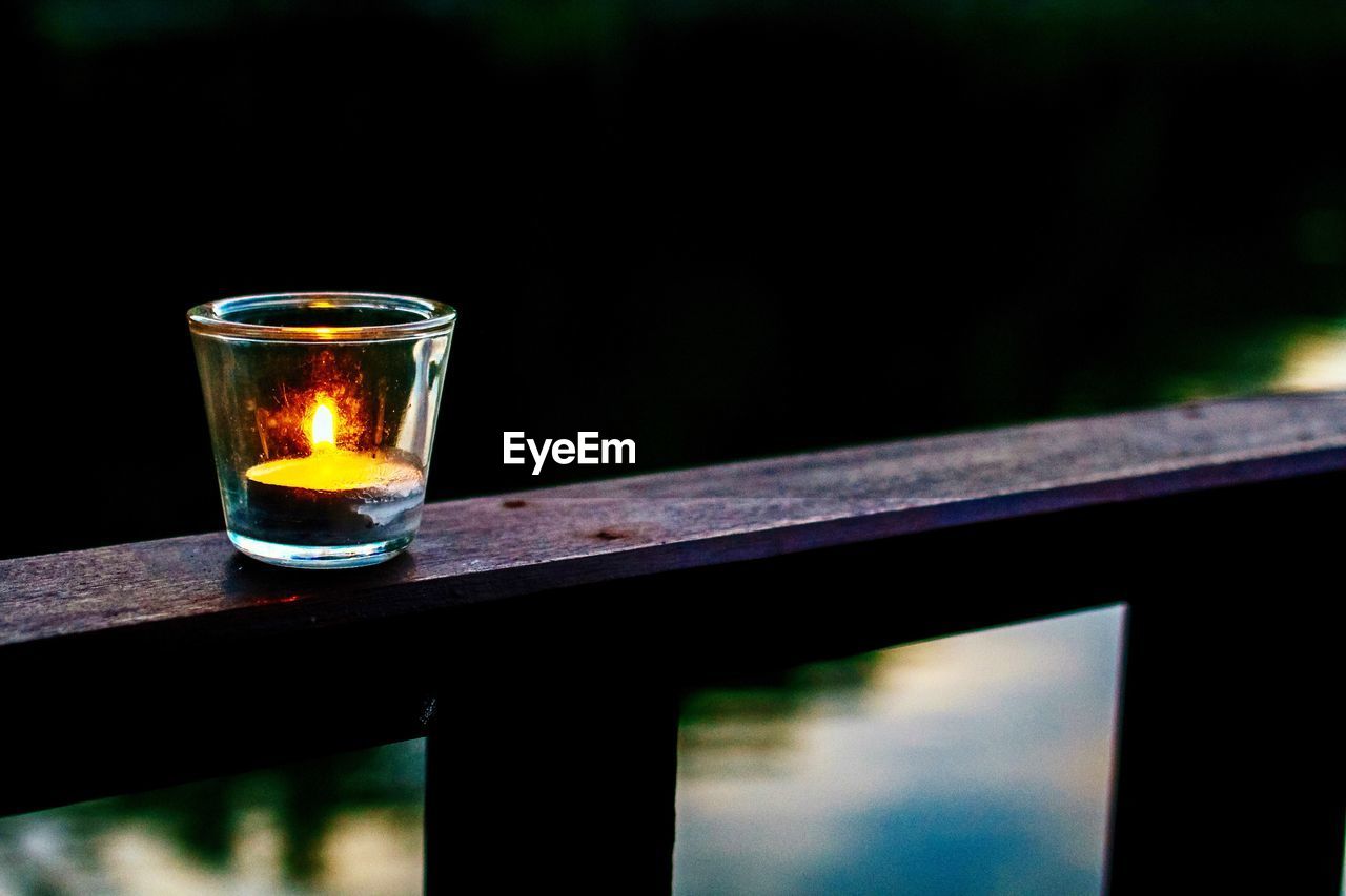 Illuminated tea light candle on railing at dusk