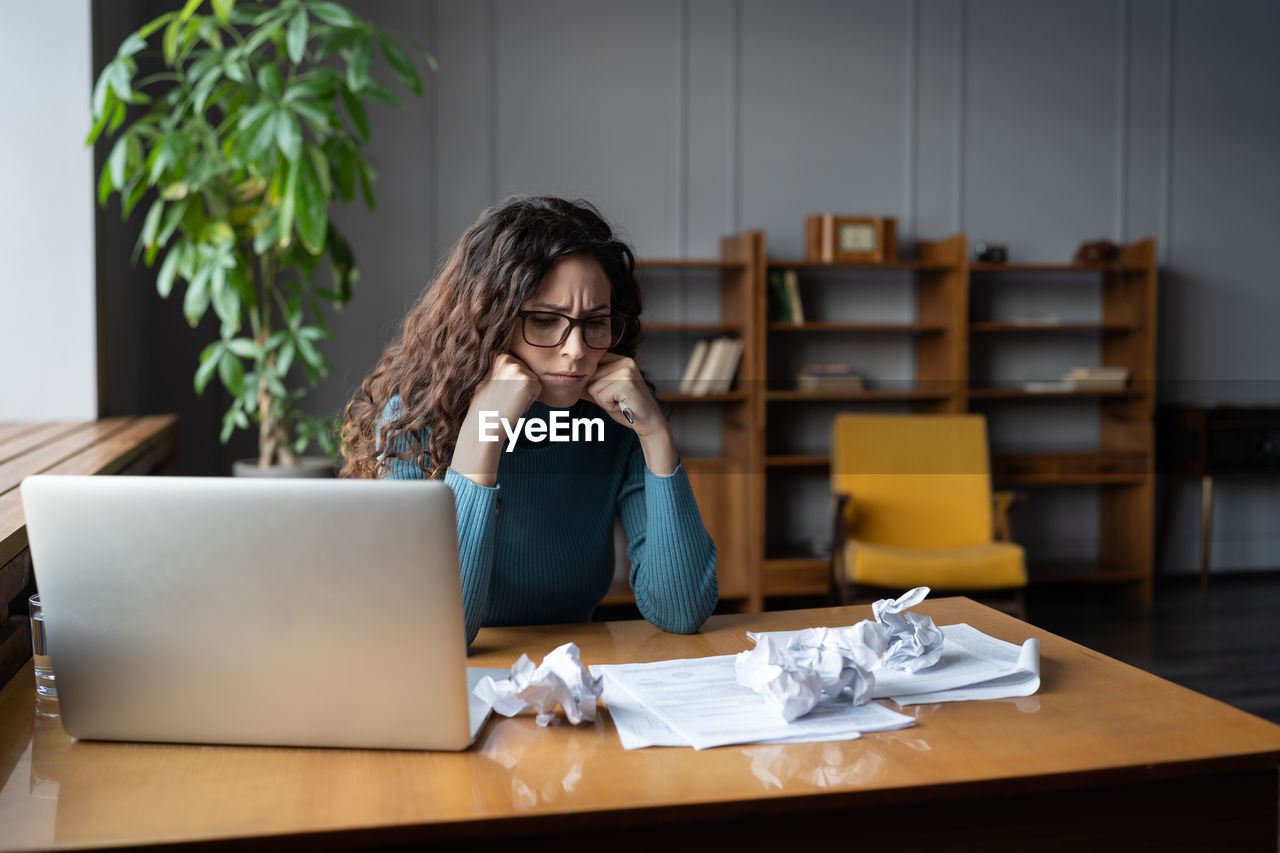 Frowning businesswoman at desk look at crumpled papers. office worker or writer tired of paperwork