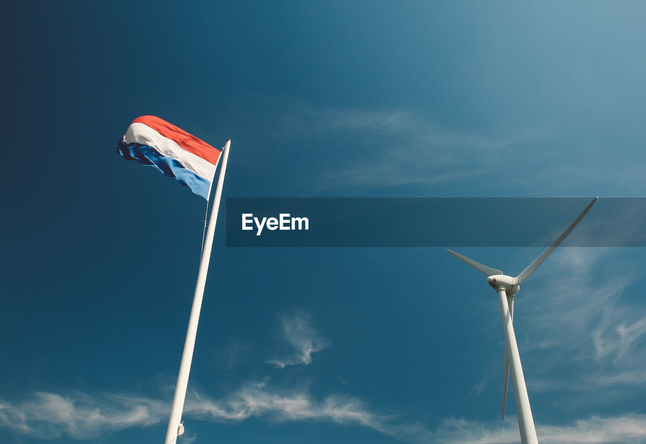 Low angle view of wind turbine and dutch flag against blue sky