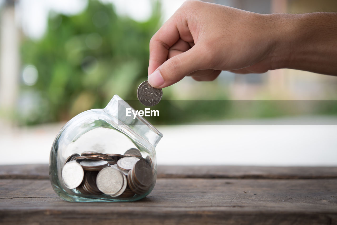 Close-up of person putting coin in jar on table