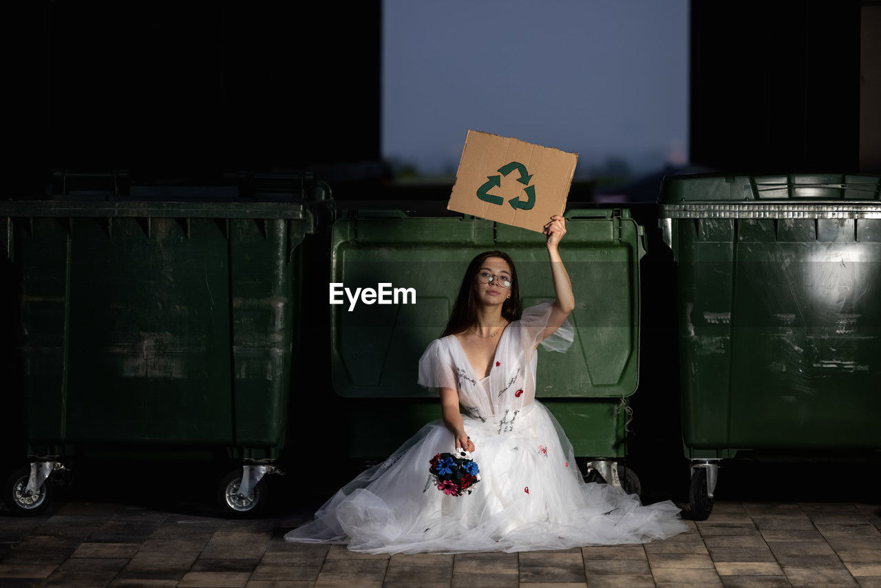 Beautiful young bride in her wedding dress holding a sign that says save the world and recycling