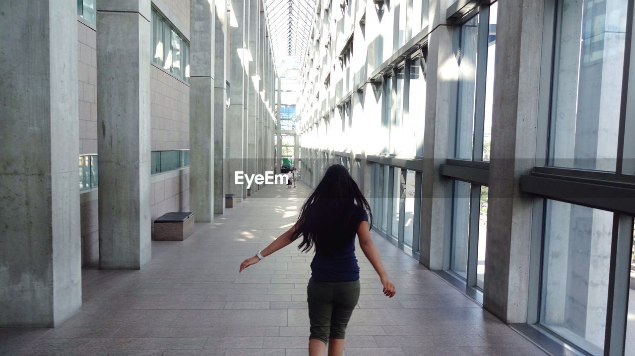 REAR VIEW OF WOMAN WALKING IN CORRIDOR OF BUILDING