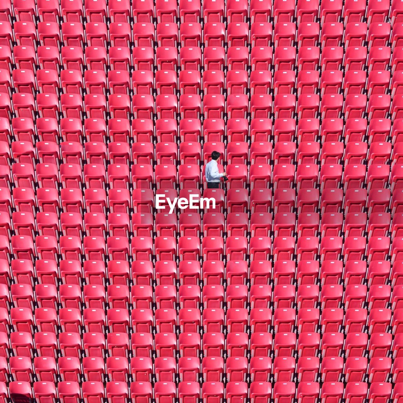 Man standing amidst red chairs at stadium