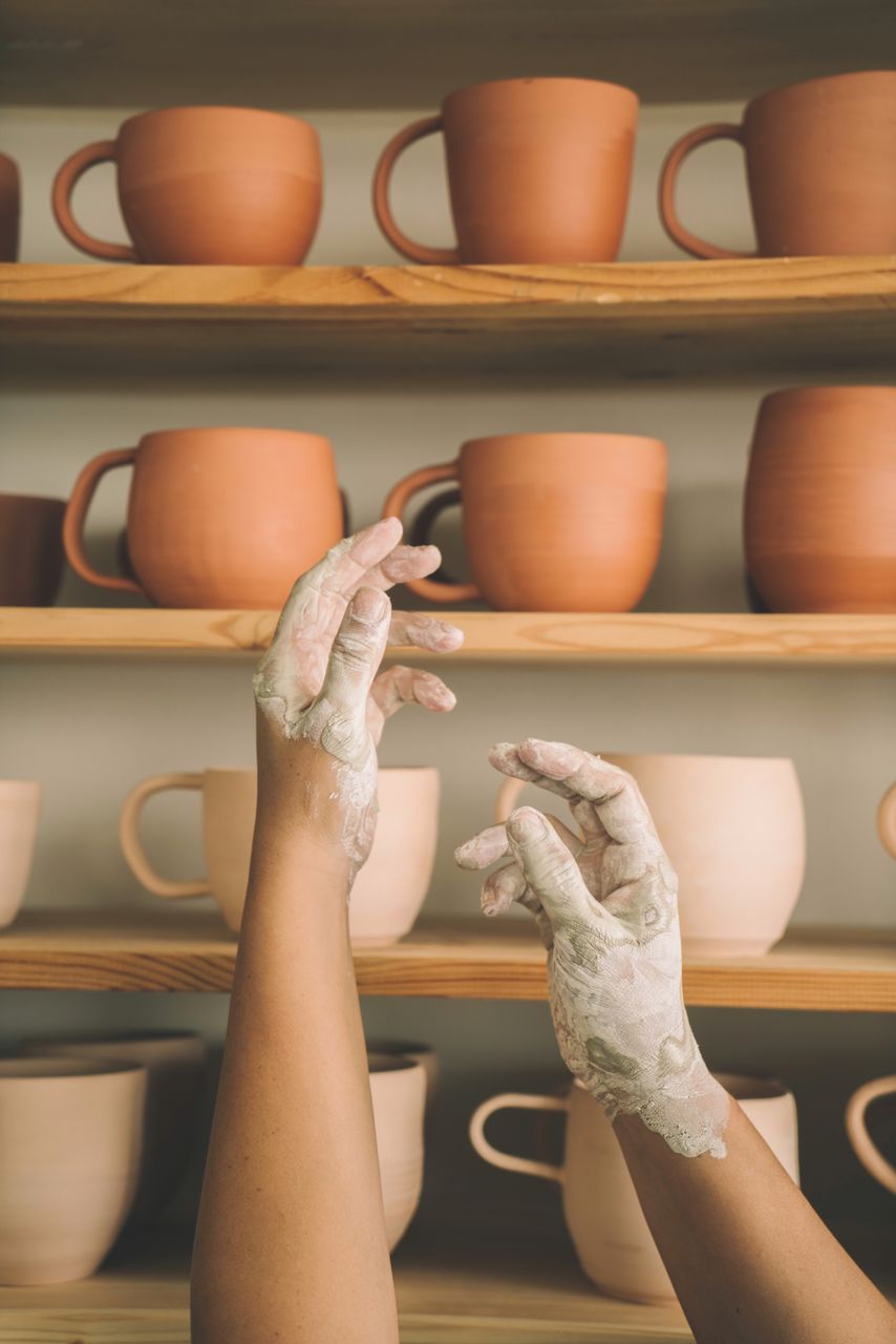 Cropped hands of potter by shelf in workshop