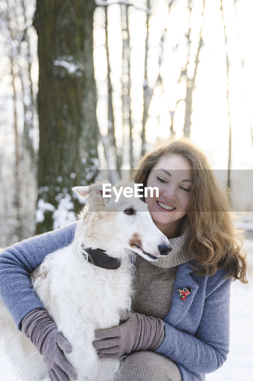 Happy mature woman with white greyhound dog in winter park