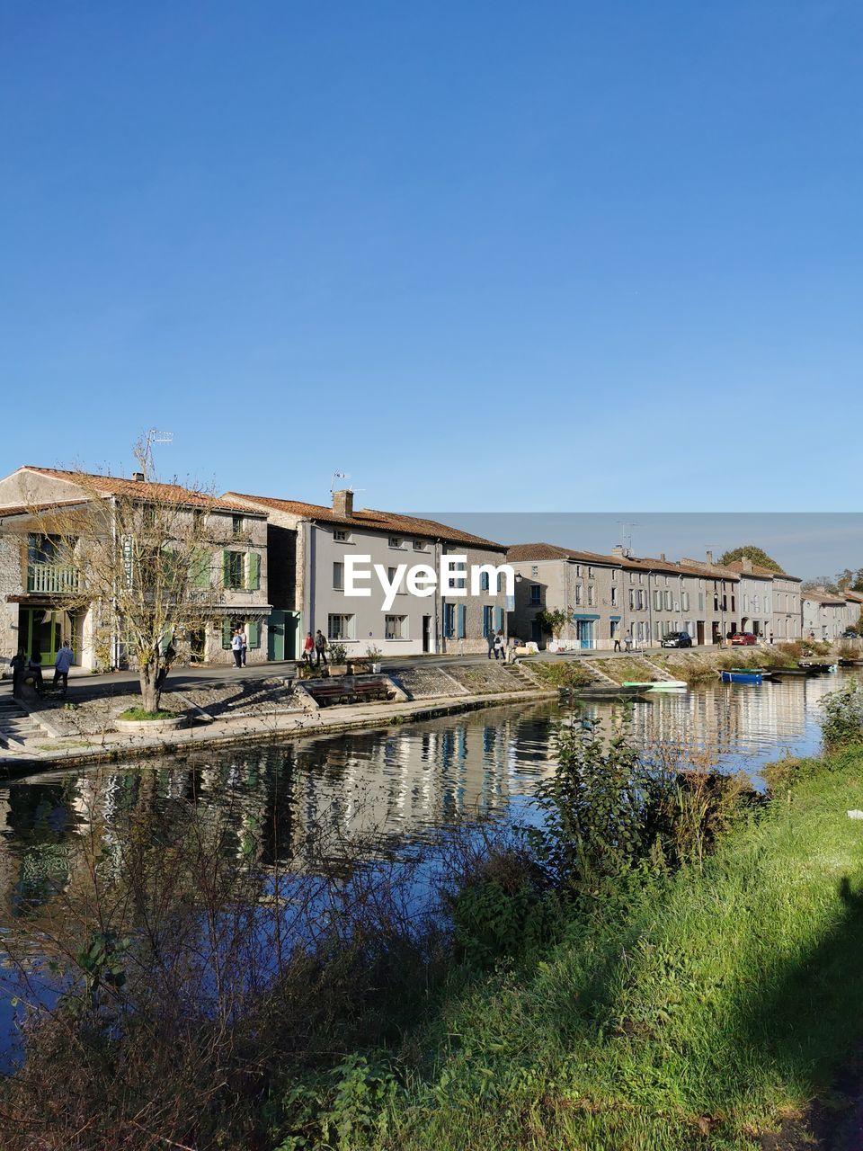 Buildings by river against clear blue sky