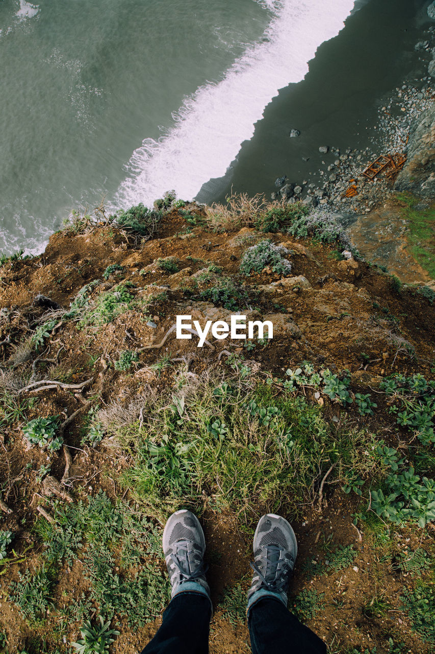 Low section of person standing on cliff by sea