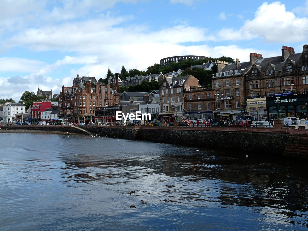 View of buildings by river against cloudy sky