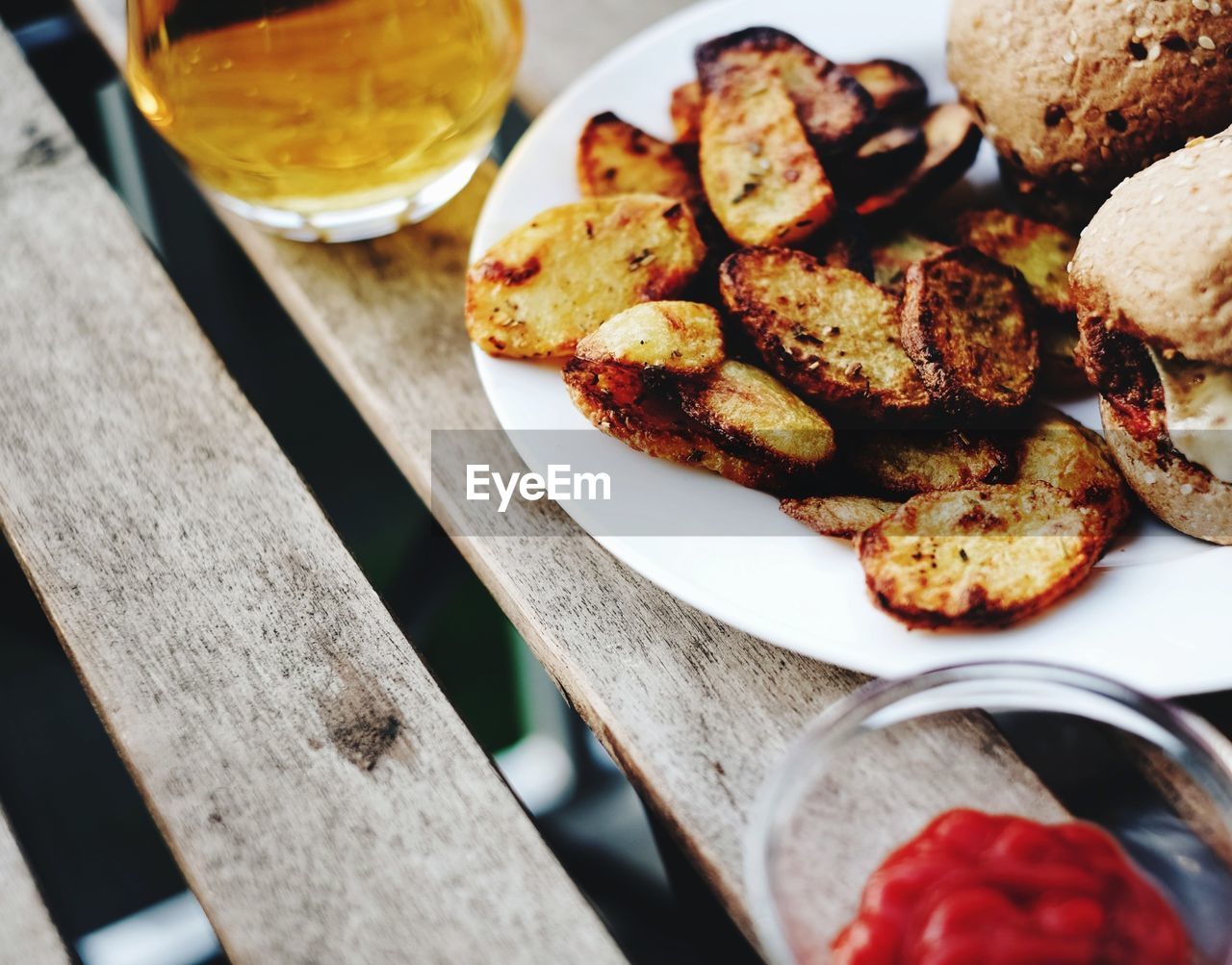 High angle view of prepared potatoes with burgers and beer on table