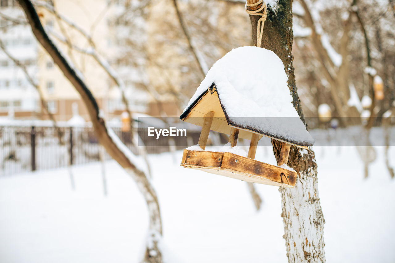 CLOSE-UP OF SNOW COVERED BIRDHOUSE ON FIELD AGAINST TREES