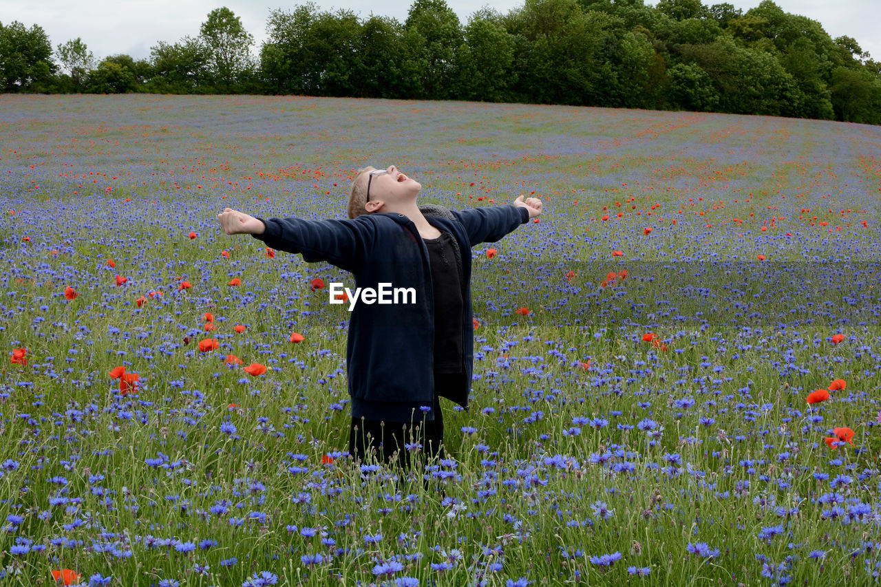 Full length of boy standing by flowers on field