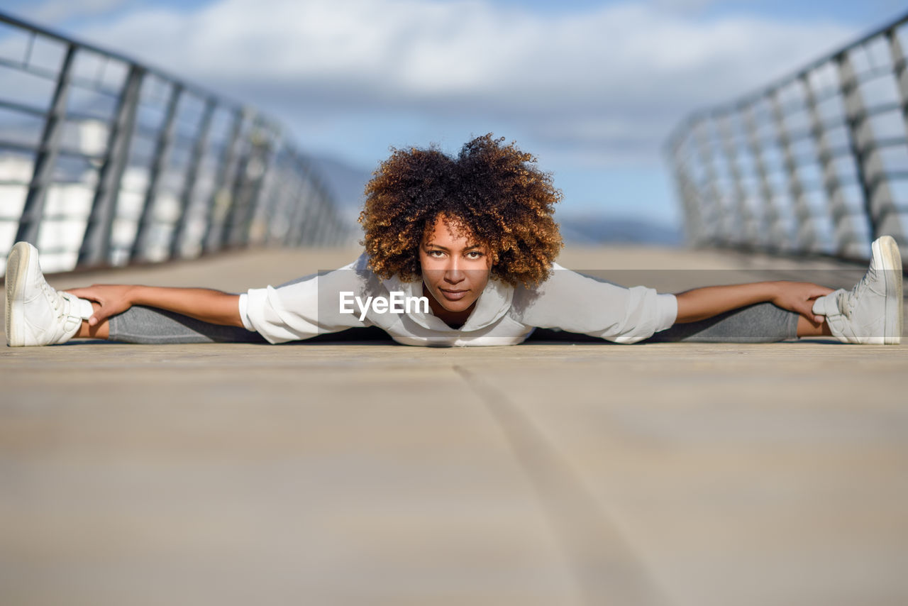 Portrait of smiling young woman with frizzy hair exercising on footbridge