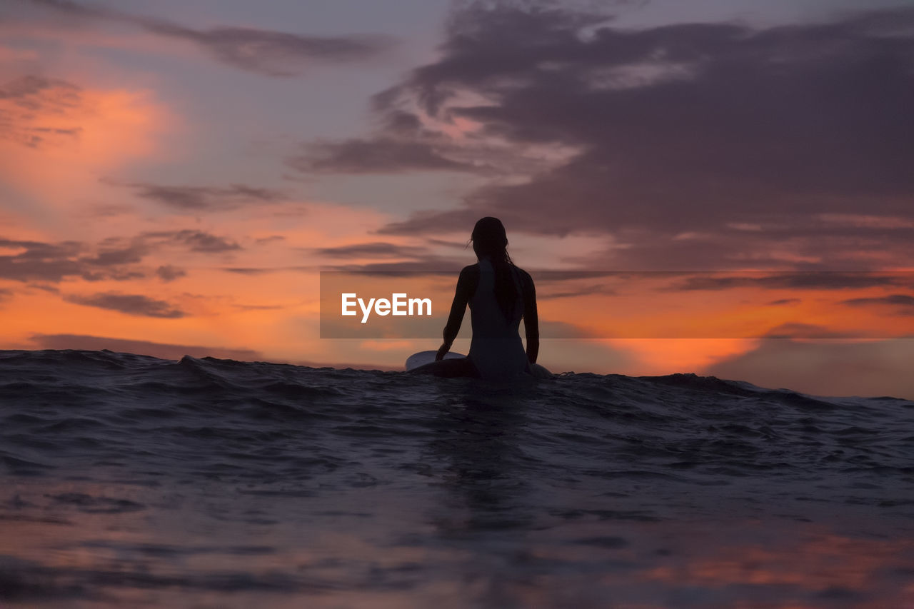 Female surfer sitting on surfboard in sea during vacation