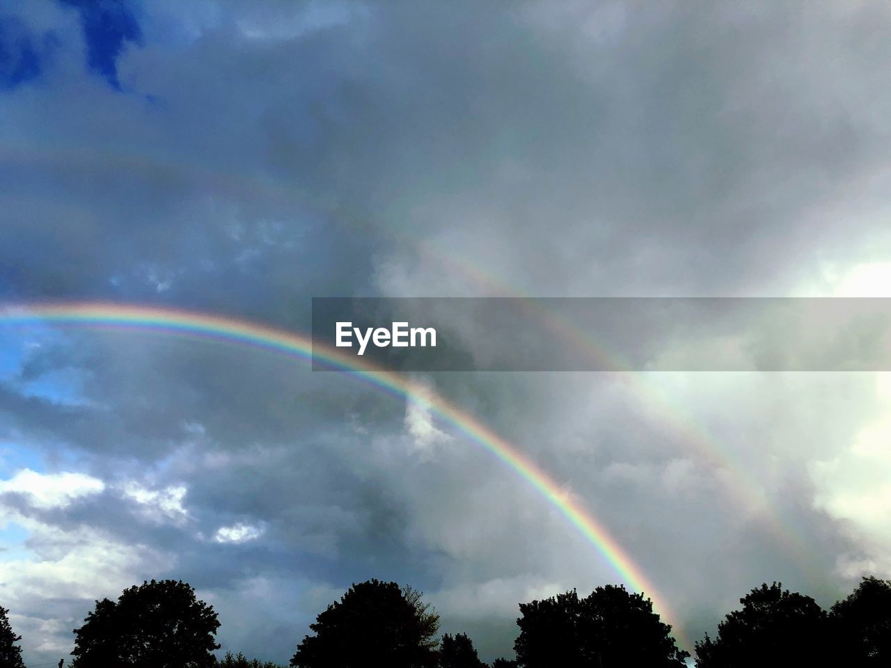 LOW ANGLE VIEW OF RAINBOW AGAINST CLOUDY SKY