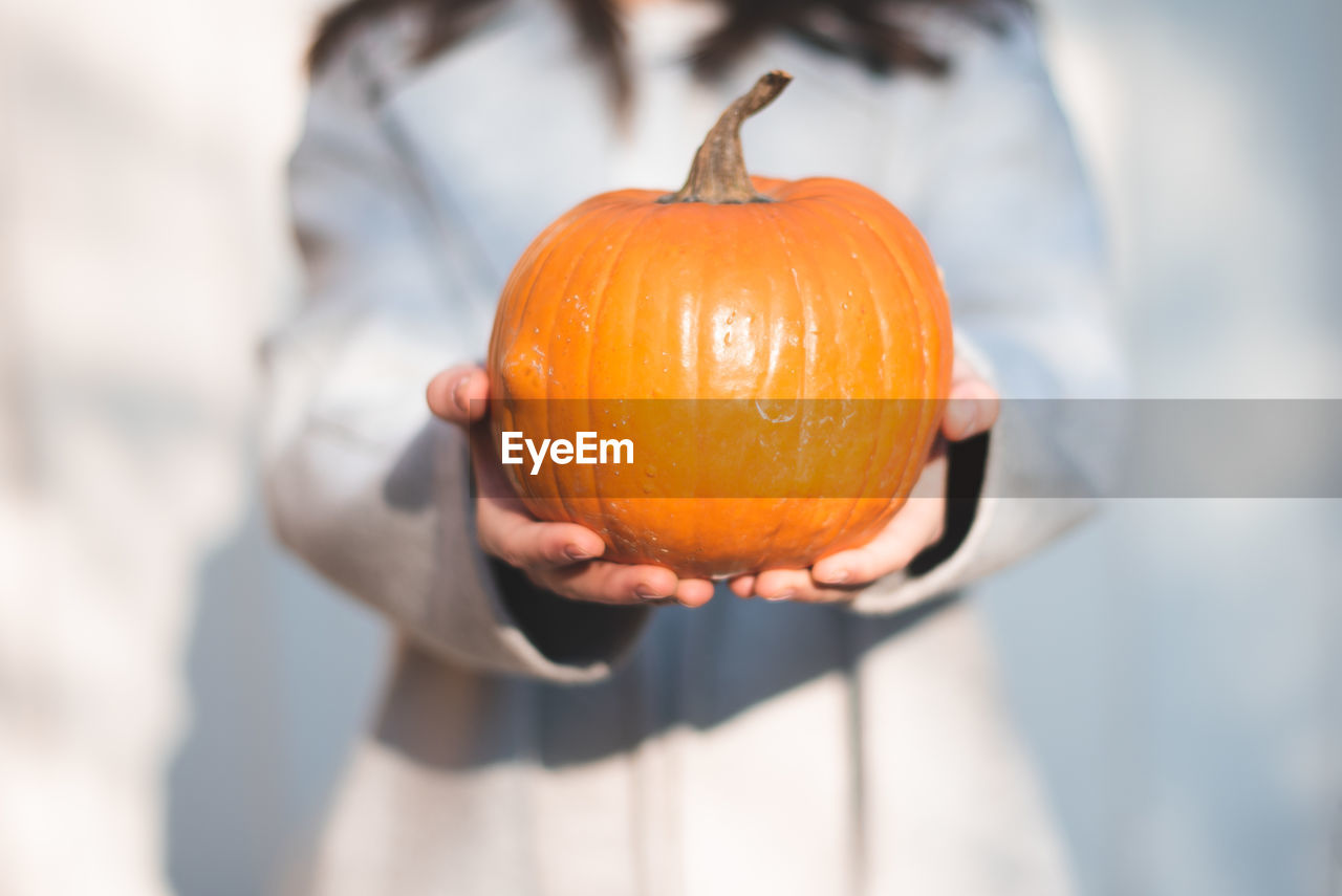 CLOSE-UP OF WOMAN HOLDING PUMPKIN AGAINST ORANGE FLOWER