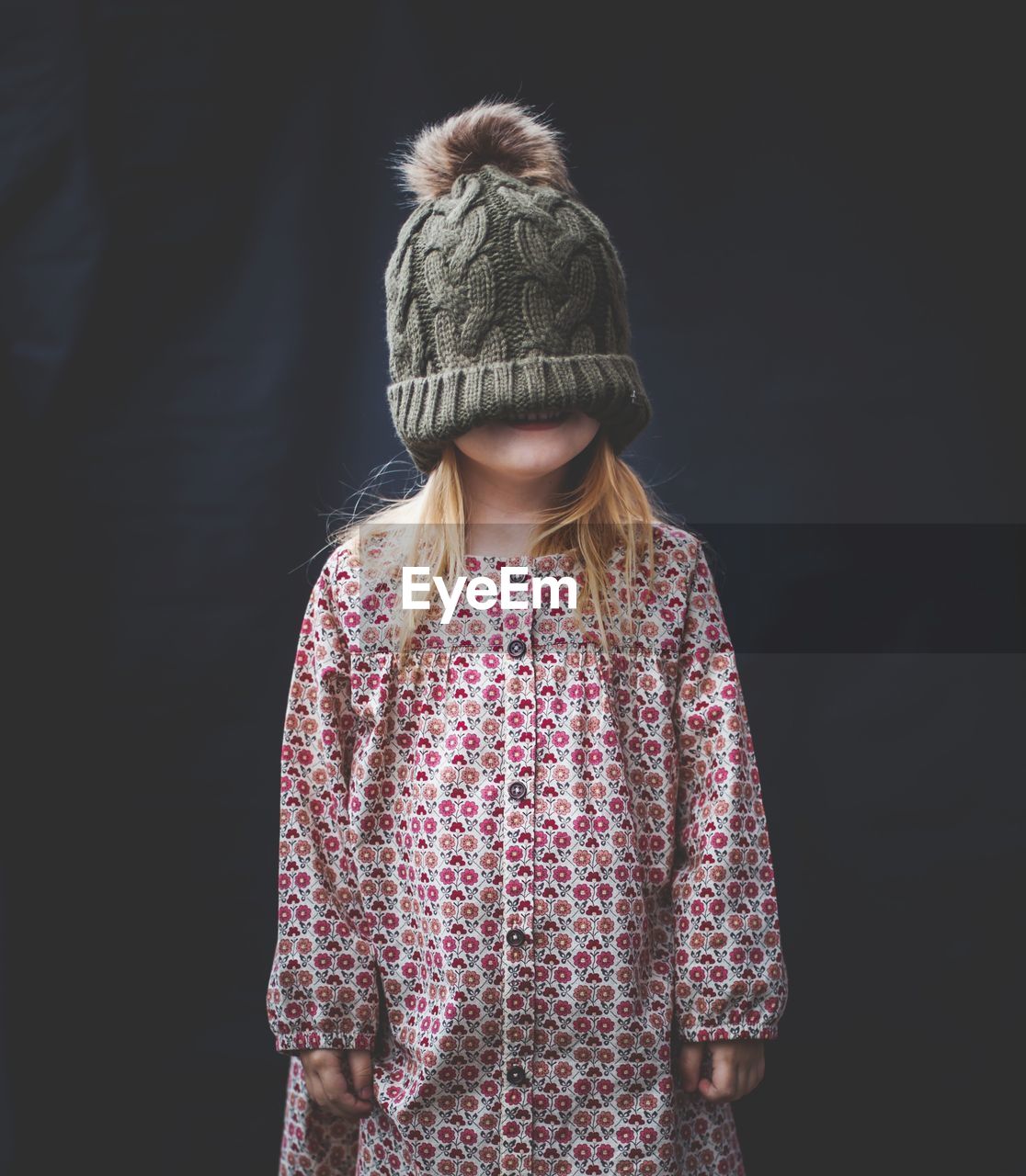 Girl wearing knit hat while standing against black background