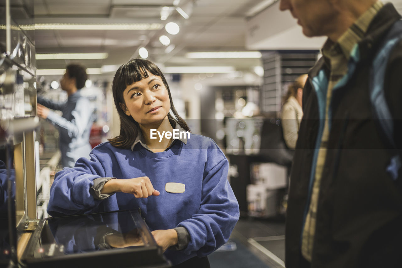 Saleswoman looking at mature customer while standing in electronics store