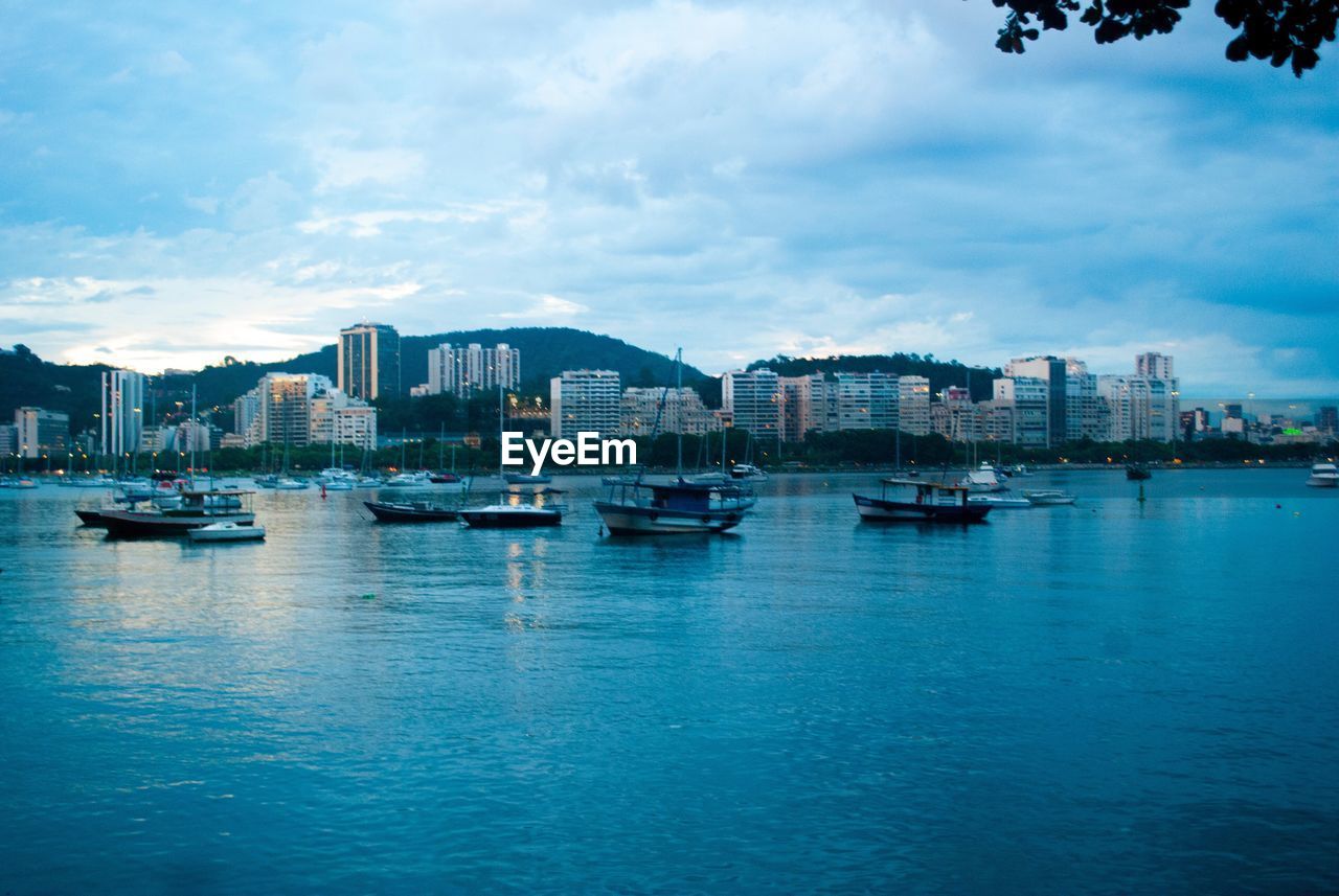 Boats in sea by cityscape against sky